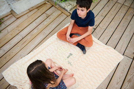 A boy and a girl enjoying a board game on a wooden deck. Relaxed outdoor atmosphere with a cozy...