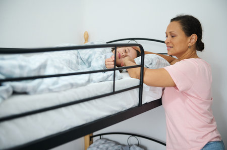 A tender moment with a mother ensuring her child is comfortable asleep in a top bunk bed, emphasizing family and care.の写真素材