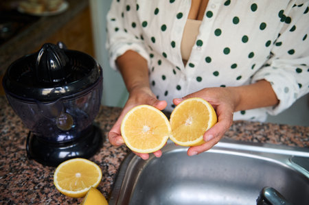 A woman holds halved oranges over a kitchen counter with a juicer, ready to make fresh orange juice.の写真素材