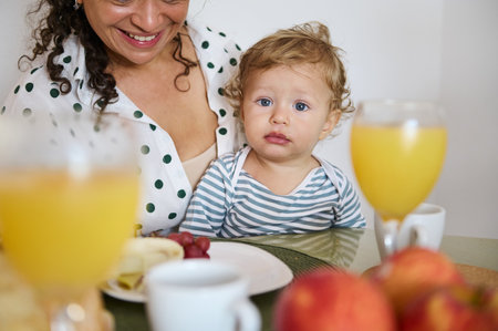 A cozy breakfast scene where a mother and her young child share a meal. The table is adorned with fresh fruit and juice, capturing a loving family moment.の写真素材