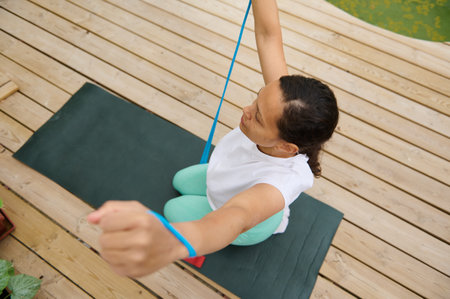 Woman performing yoga with a resistance band on a deck, highlighting fitness and tranquility in an...