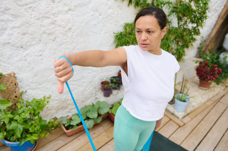 A woman is working out with a resistance band in a garden, demonstrating strength, focus, and a...