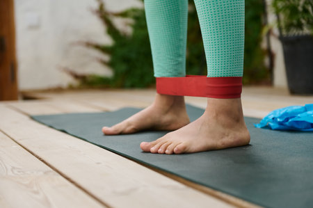 Close-up of feet using a red resistance band on a yoga mat outdoors, emphasizing fitness and wellness activities.の写真素材