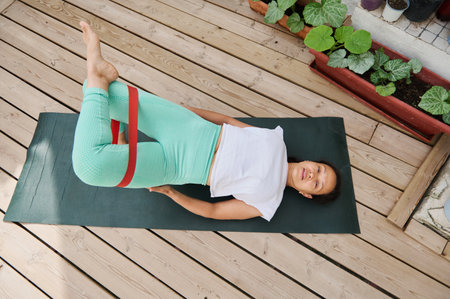 A woman performs Pilates exercises with resistance bands on a yoga mat outdoors, emphasizing fitness...