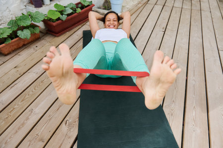 A woman smiles while performing a leg workout with a resistance band on a yoga mat in a serene...