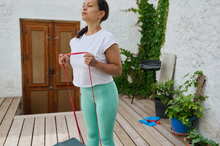 Woman practicing fitness with resistance band outdoors. Focus on wellness, strength, and healthy...