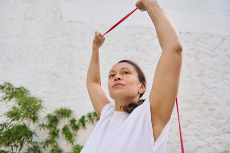 Focused woman performing resistance band workout outdoors, emphasizing fitness, strength, and...