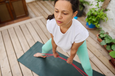 A woman demonstrates resistance band exercises on a yoga mat outdoors, focusing on strength and...