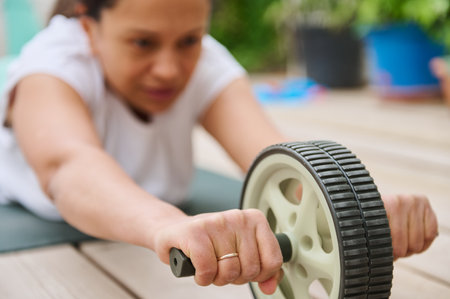 A woman using an ab roller for core exercise on a mat outdoors. Focused on fitness and strength training.の写真素材