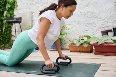 Middle-aged woman exercising with push-up bars outdoors, showcasing strength and dedication to a...