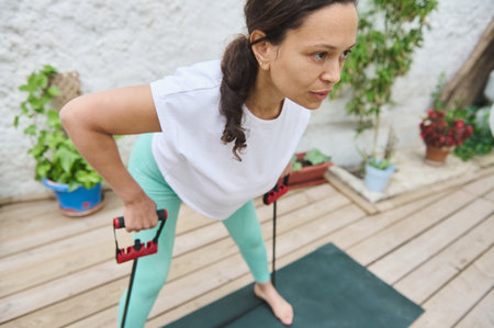 Woman engaged in a fitness routine using resistance bands on a mat outdoors, emphasizing strength...