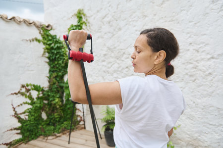 A woman performs resistance band exercises outside, emphasizing strength and fitness. The setting...