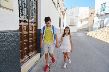 A young boy and girl hold hands while walking down a peaceful residential street, showcasing sibling bond and companionship.の写真素材