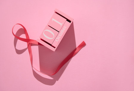 A pink calendar block showing October 1st, accompanied by a ribbon on a pink background, representing the beginning of breast cancer awareness month.の写真素材