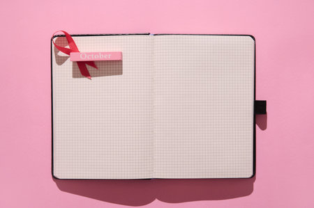 An open grid notebook with a red ribbon bookmark labeled 'October,' set against a vibrant pink background, perfect for planning and creativity.の写真素材