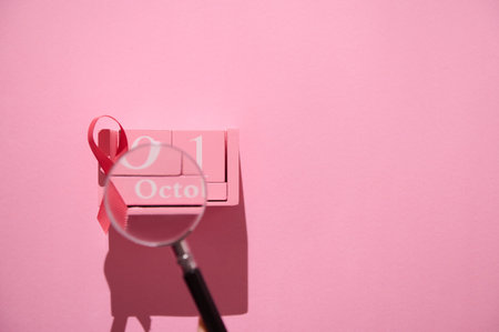 Pink October calendar with a ribbon for breast cancer awareness and magnifying glass on pink background, symbolizing health awareness.の写真素材