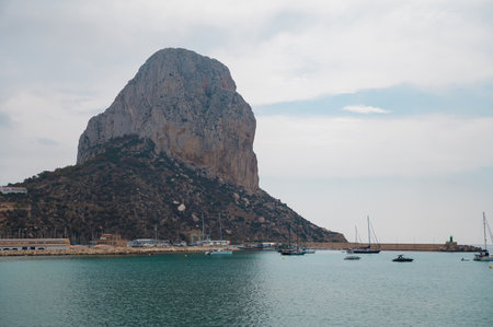 A tranquil image of Penon de Ifach towering over the serene coastal waters in Calpe, Spain, with...