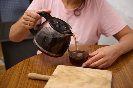 A person pours fresh coffee from a pot into a glass, creating a warm and inviting atmosphere,...