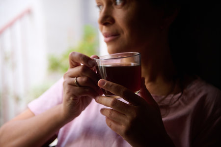 Woman gazing thoughtfully while sipping tea, capturing a serene and reflective moment indoors.
