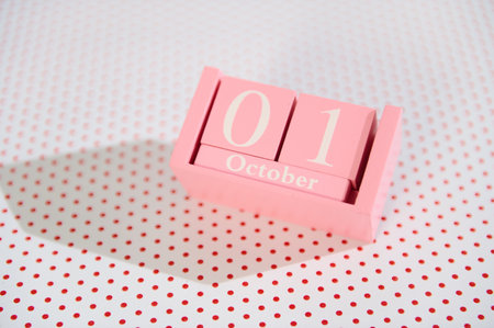 Pink wooden calendar block showing October 1st on a dotted background, ideal for autumn and event...