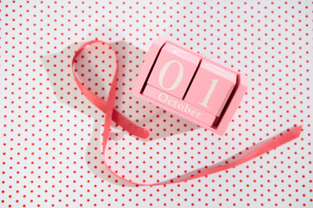 Pink cube calendar displaying October 1st, accompanied by a ribbon on a polka-dot background.の写真素材