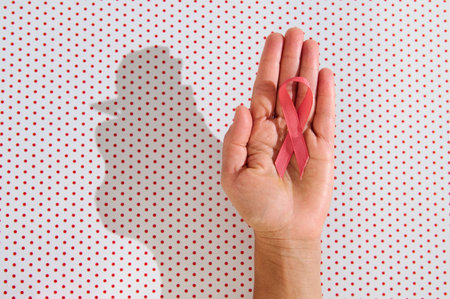 Close-up of a hand holding a red awareness ribbon against a red polka dot background, symbolizing support and awareness.の写真素材