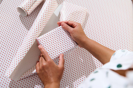 Hands wrapping a gift with white and red polka dot wrapping paper, highlighting the art of...