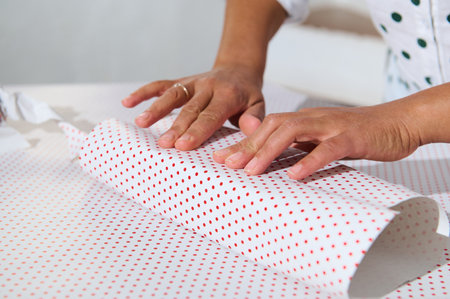 Hands carefully wrapping a gift with red polka dot paper, symbolizing care and celebration.