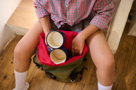 Close-up of a person packing camping mugs into a backpack, ready for an outdoor adventure.