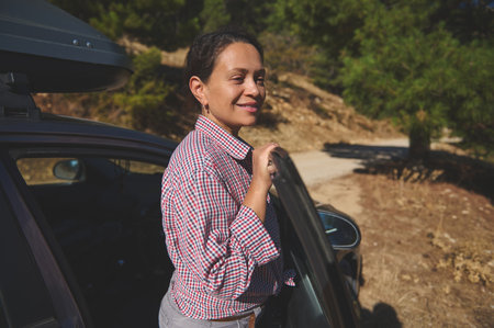 A woman stands by a car in a scenic outdoor setting, embracing nature and enjoying a road trip.の写真素材