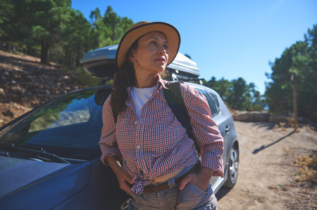 Woman with a backpack stands by her car in a scenic forest, embracing adventure and nature during a...