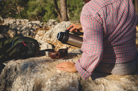 A person pours coffee from a thermos into cups amidst a natural rocky scenery, enjoying a tranquil outdoor break.の写真素材