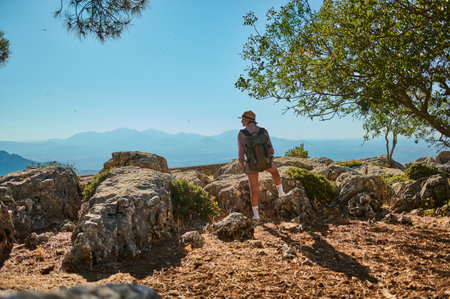 A hiker with a backpack and hat explores a rocky trail on a mountain, surrounded by nature. The person enjoys breathtaking views and the serenity of the outdoors under a clear blue sky.の写真素材