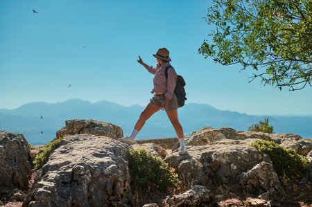 A woman in casual hiking attire explores a rocky mountain terrain, surrounded by breathtaking landscapes. Her adventurous spirit is evident as she immerses herself in nature's beauty.の写真素材