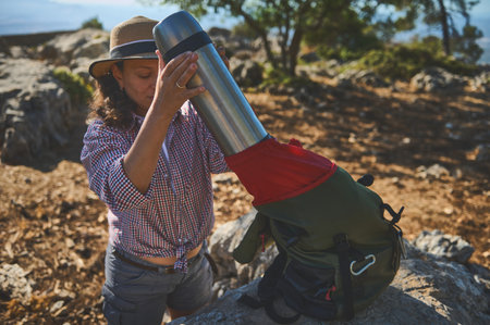 A woman equips herself for a hiking adventure, packing a large thermos into her backpack, in a rocky...