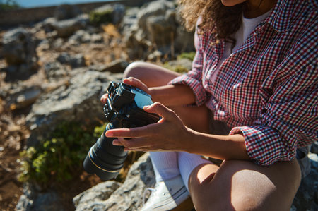 A woman in a plaid shirt sits on rocky terrain, adjusting her camera settings. The scene captures...