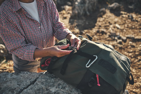 A woman adjusts the straps of her green backpack while hiking in a rocky outdoor setting, showcasing...