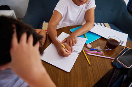 A mother helps her child with homework, showing patience and guidance. Pencils and notebooks are...