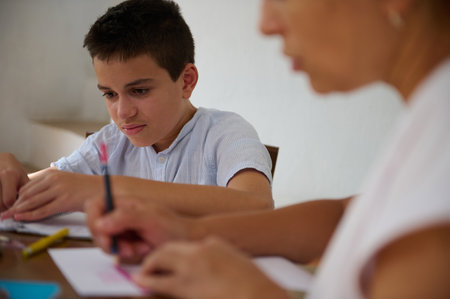 A focused young boy works on homework with an adult in a supportive study environment, emphasizing education and teamwork.の写真素材
