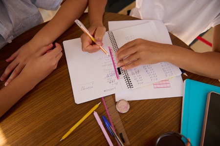 Close-up of students working together on math problems in a notebook. Cooperative learning, teamwork, and problem-solving are emphasized in this study session.の写真素材