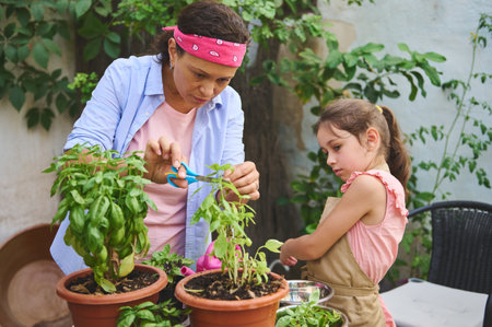 A mother and her daughter are engaged in gardening, trimming plants in an outdoor garden. The scene portrays a delightful bonding experience while learning and working together with nature.の写真素材