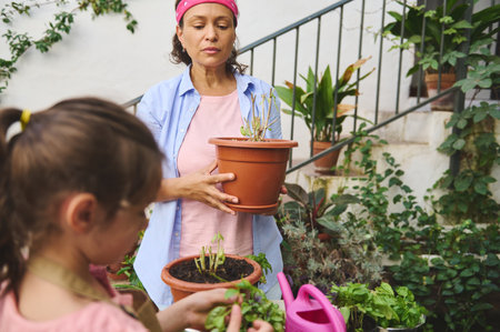 A mother and daughter enjoy quality time gardening together on a sunny day. The duo is seen with potted plants, surrounded by green foliage, expressing their love for gardening and nature.の写真素材