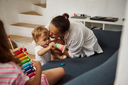 A mother engages joyfully with her young child in a cozy living room. The child is playing with a colorful xylophone, showcasing a nurturing family atmosphere.の写真素材