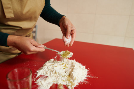 A person in an apron prepares dough on a red tabletop. The scene captures the warmth and creativity of homemade cooking, emphasizing the mixing process with flour and other ingredients.の写真素材