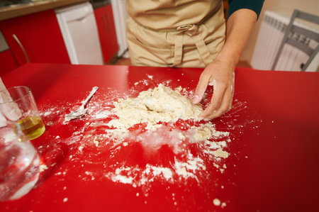 A close-up of a person's hands kneading dough on a vibrant red kitchen countertop. The scene conveys the art of baking, focused on the process of creating homemade bread or pastries.の写真素材