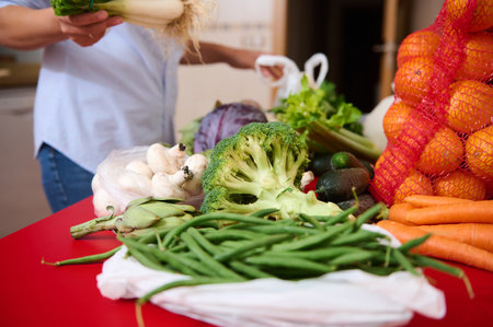 A vibrant selection of fresh vegetables including broccoli, artichokes, and mushrooms are displayed on a red kitchen table, highlighting healthy eating and organic produce.の写真素材
