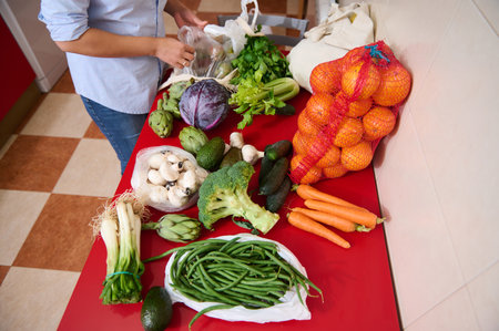 A person arranges a variety of fresh vegetables and fruits on a red kitchen counter. The colorful...