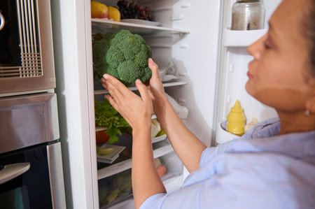 A woman organizing fresh vegetables in her refrigerator, highlighting a healthy lifestyle. The image features vibrant greens, symbolizing nutrition and wellness, with a focus on fresh broccoli.の写真素材
