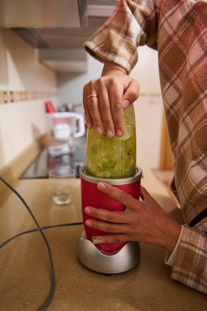 Close-up of a person using a blender to prepare a fresh green smoothie in a cozy kitchen setting. The image captures the essence of healthy living and homemade nutrition routines.の写真素材