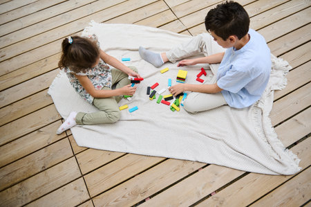 Two children are engaging in creative play with colorful blocks on a wooden deck. They are sitting...